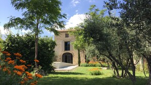 A stone building with a central archway, surrounded by lush greenery and orange flowers. -  Mas Le Félibre **** (Caumont-sur-Durance)