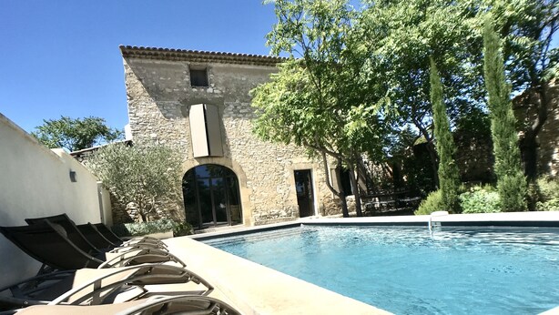 A pool area with lounge chairs, a stone building with an arched doorway, and surrounding greenery. -  Mas Le Félibre **** (Caumont-sur-Durance)