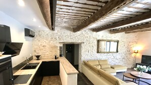 A modern kitchen with a built-in island, a stone wall, and a cozy seating area with a sofa and armchairs. -  Mas Le Félibre **** (Caumont-sur-Durance)