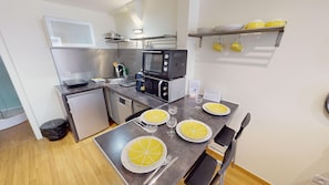 Eine kleine Küche mit Mikrowelle, Toaster und kleinem Kühlschrank. Zwei Esstische sind mit gelben Tellern und Weingläsern gedeckt.