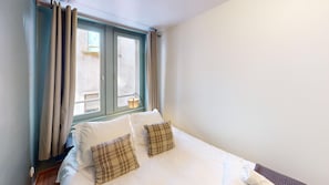 Une chambre à coucher avec un lit, deux oreillers, une fenêtre avec des rideaux et une vue sur l’extérieur.