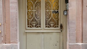Uma porta bege com um painel de vidro decorativo, um número '6' em destaque acima e uma pequena caixa de correio à direita.