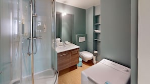 Une salle de bain avec une douche à parois de verre, un lavabo avec un miroir, des toilettes et un lave-linge.