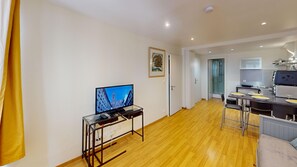 A modern living room with a flat-screen TV, a dining area with a bar, and a kitchen with a stove.