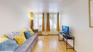 A modern living room with a sofa, a TV on a stand, and a window with curtains.