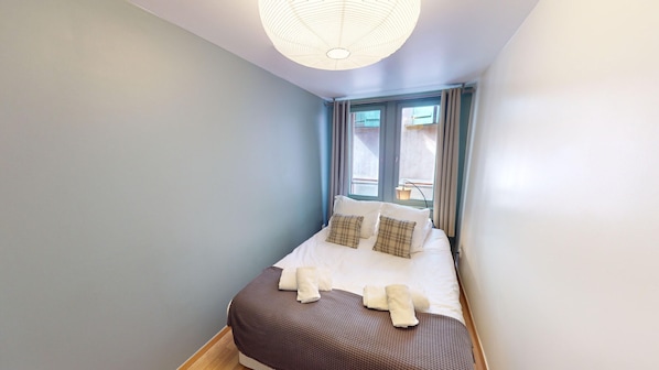 Ein Schlafzimmer mit einem Bett, Kissen, einem Nachttisch und einem Fenster mit Vorhängen.
