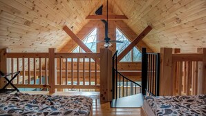 A wooden cabin with a loft bedroom, a staircase, and a view through the windows.