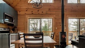 A wooden cabin interior with a dining table, chairs, a stove, and a kitchen area with a microwave and stove.