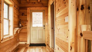 A wooden cabin interior with a door, windows, and a wooden bench.