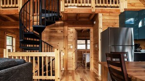 A cabin interior with a spiral staircase, wooden floors, a dining area, and a kitchen with a refrigerator.