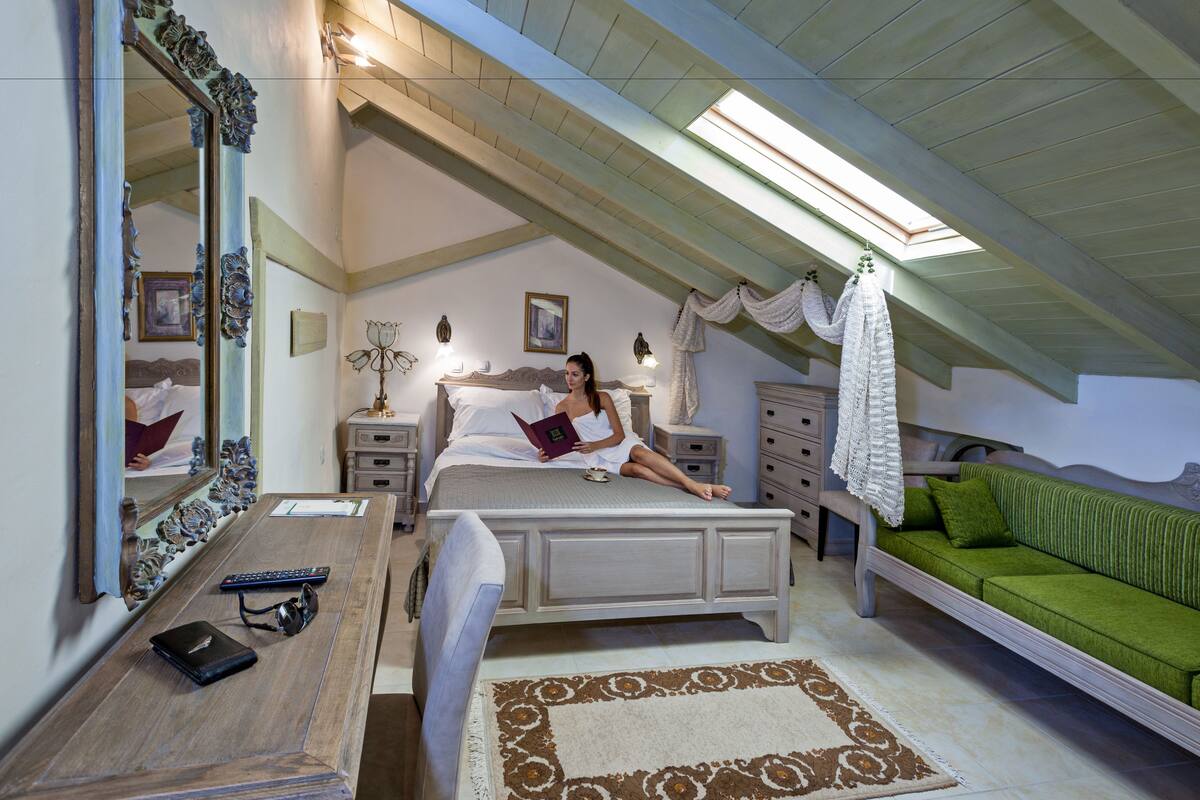 Un dormitorio con una cama, mesitas de noche, un espejo, un sofá verde y una alfombra estampada.