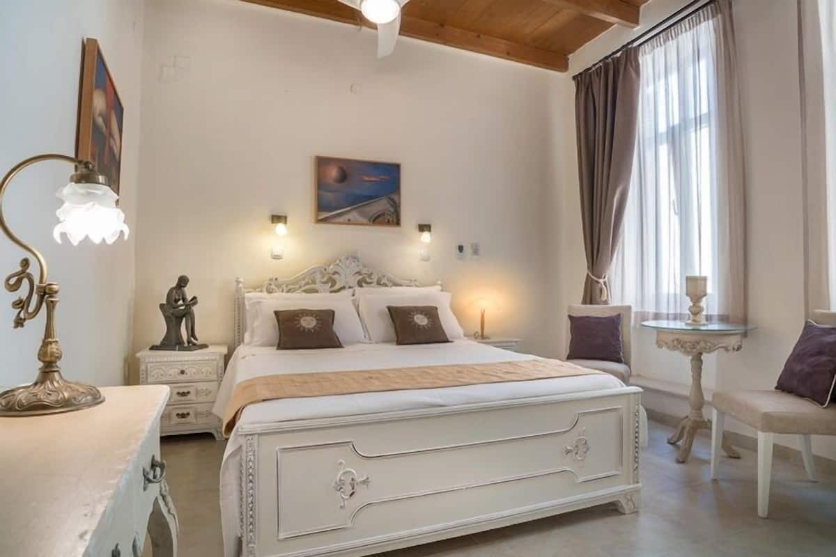 Un dormitorio con una cama grande, lámparas de noche, una mesita y una silla.