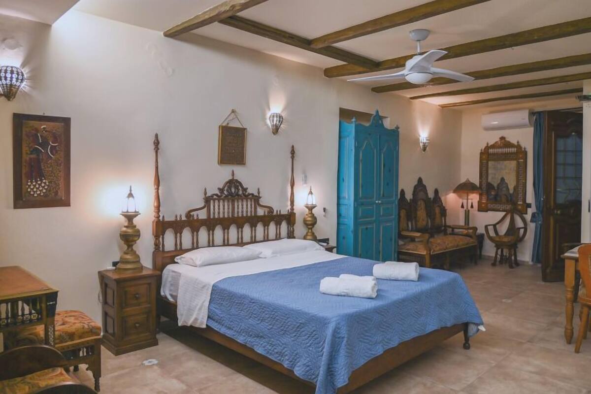 Un dormitorio tradicional con cama de madera, colcha azul y ventilador de techo.