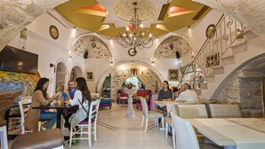 Un restaurante con techos altos en arco, una araña y una fuente central. Mesas y sillas dispuestas para comer.
