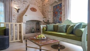 Una sala de estar acogedora con una pared de piedra, un sofá verde, una mesa de centro de madera con fruta y una chimenea.