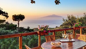 A wooden deck with a table set for dining, overlooking a scenic view of the sea and a mountain. - Peter's House (Sorrento)