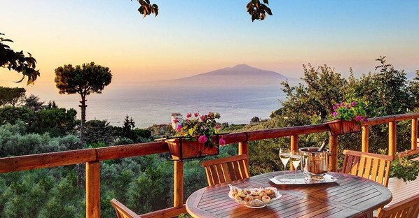 Une terrasse en bois avec une table dressée pour le repas, offrant une vue panoramique sur la mer et une montagne.