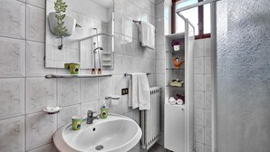 A bathroom with a white sink, a mirror, a shower, and a toilet. There are shelves with toiletries and towels. - Peter's House (Sorrento)