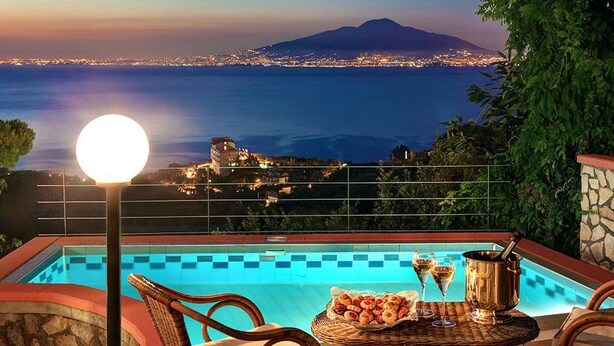 A poolside view with a clear view of the sea and a mountain in the background, a wicker chair, a table with snacks and drinks, and a lamp post. - Peter's House (Sorrento)