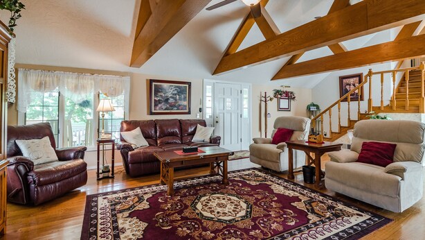 A spacious living room with a wooden ceiling, a large rug, leather sofas, and a staircase. - Mountain Majesty ~ Country elegance at its best! (Huntsville)