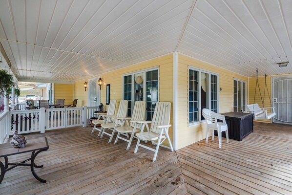 A covered porch with wooden flooring, white chairs, a table, and a swing chair.