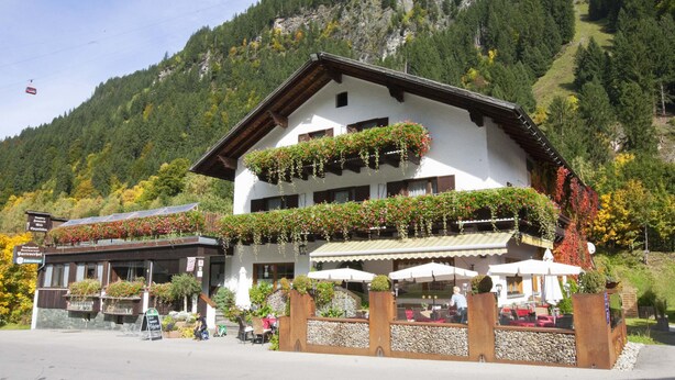 A mountain lodge with a balcony adorned with flowers, outdoor seating, and a view of the surrounding forest. - Partenerhof (Gaschurn)