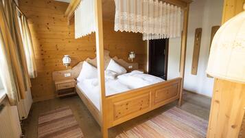 A wooden four-poster bed with white linens, a nightstand with a lamp, and a wooden floor.