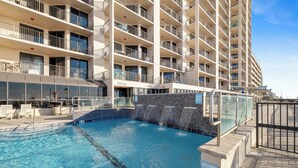 A swimming pool with a no-climbing, no-humping sign, surrounded by a multi-story building with balconies and a glass railing.