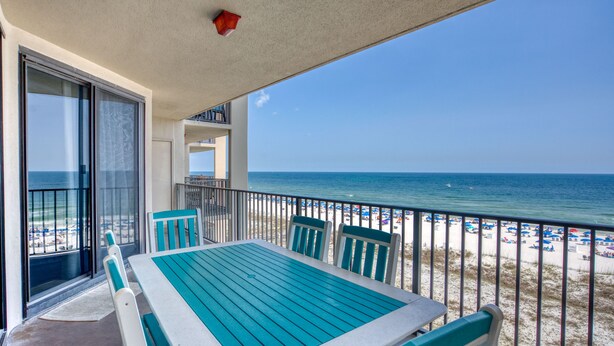 A balcony with a table and chairs, overlooking a beach with umbrellas and the ocean.