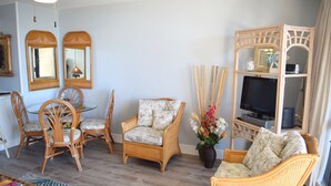 A living room with wicker furniture, a glass coffee table, and a television on a stand. - Beautiful Partial Ocean View Condo with Tropical Furnishings (Kihei)