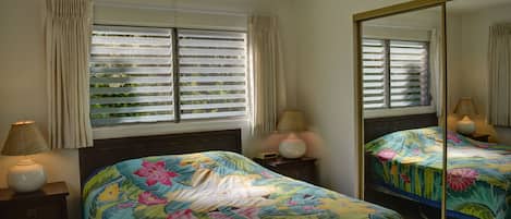 A bedroom with two beds, a large mirror, and a window with blinds.