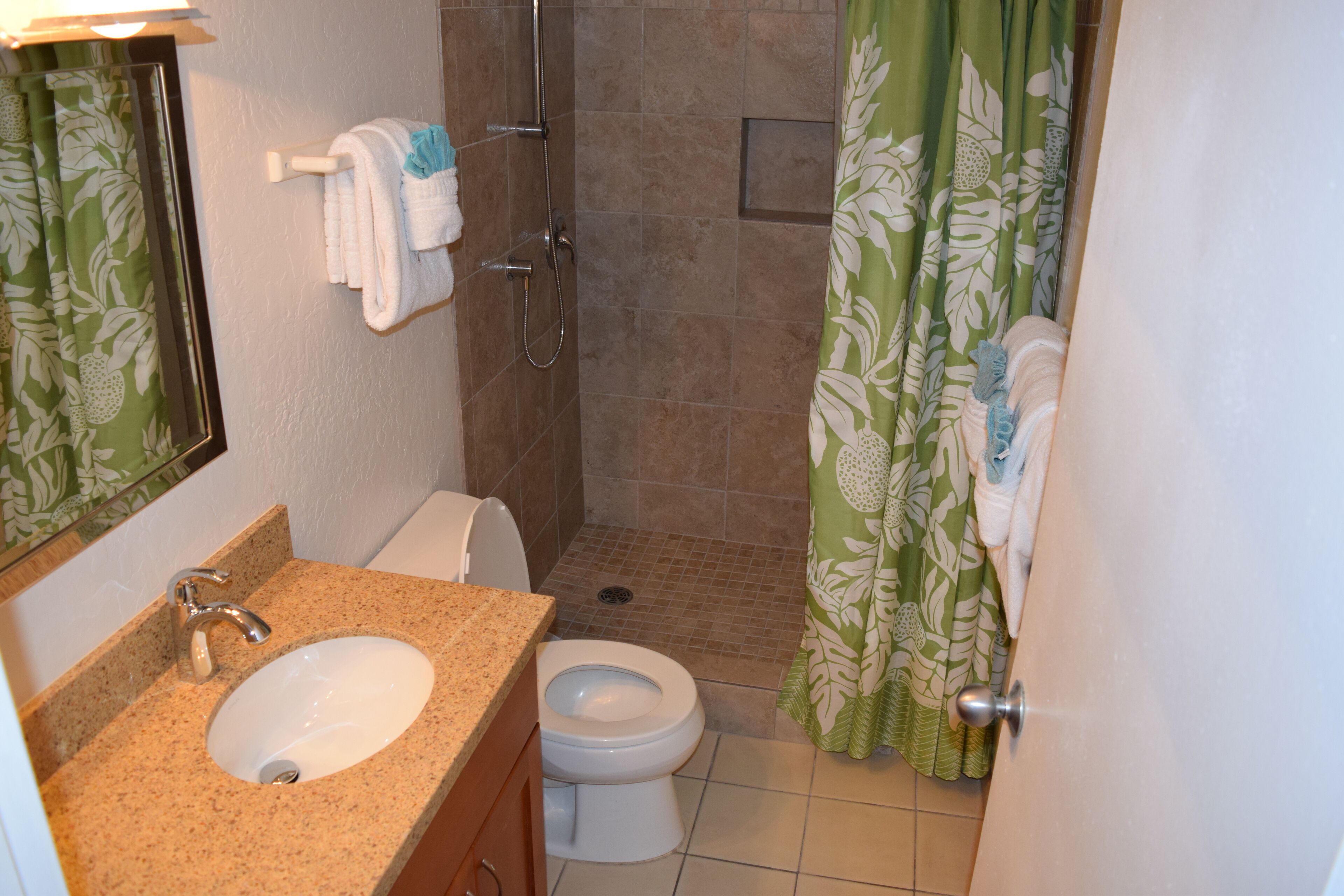 A bathroom with a sink, toilet, shower, and green floral curtains.