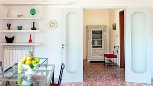 A dining area with a glass table and chairs, a fruit bowl, and a decorative cabinet with a mirror. - Skyline Sorrento (Sorrento)
