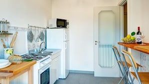 A compact kitchen with a stove, microwave, sink, and a small refrigerator. There is a dining area with a table and chairs, and a door leading to another room. - Skyline Sorrento (Sorrento)