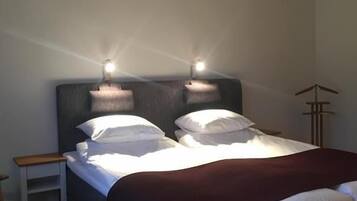 Una cama bien hecha con sábanas blancas y un cabecero oscuro, junto con una mesita de noche y una lámpara de pie.