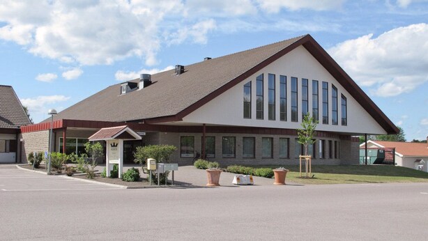 A modern building with a sloped roof, large windows, and a parking lot in front.