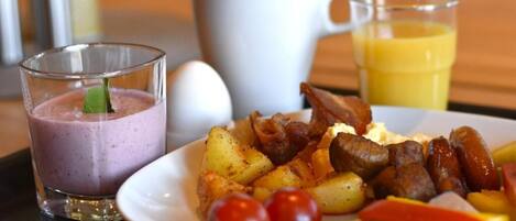 A breakfast plate with eggs, bacon, sausages, potatoes, and vegetables, accompanied by a glass of juice and a smoothie.