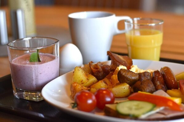 A breakfast plate with eggs, bacon, sausages, potatoes, and vegetables, accompanied by a glass of juice and a smoothie. - Munken Hotell & Konferens (Monsteras)