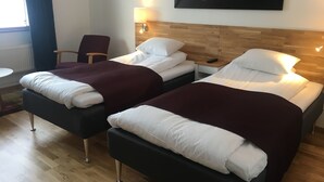 A hotel room with two beds, a chair, a table, and a painting of a sunset.