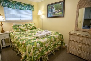 Quarto com cama, mesa de cabeceira, cômoda, abajur e quadro pendurado na parede.