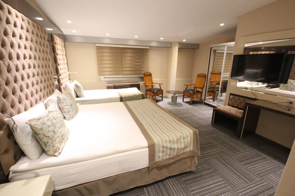 Habitación de hotel con dos camas, un escritorio con televisor, una silla y una ventana con persianas.
