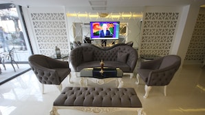 Uma sala de estar moderna com um sofá, uma mesa de centro e um banquinho. Uma televisão está montada na parede, e há um painel decorativo atrás do sofá.