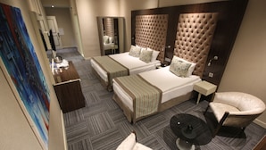 Quarto de hotel com duas camas, área de estar com uma poltrona, uma mesinha e um quadro grande na parede.