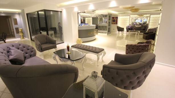 Uma sala de estar moderna com uma mesa de centro de vidro, um sofá cinza e uma poltrona estofada.