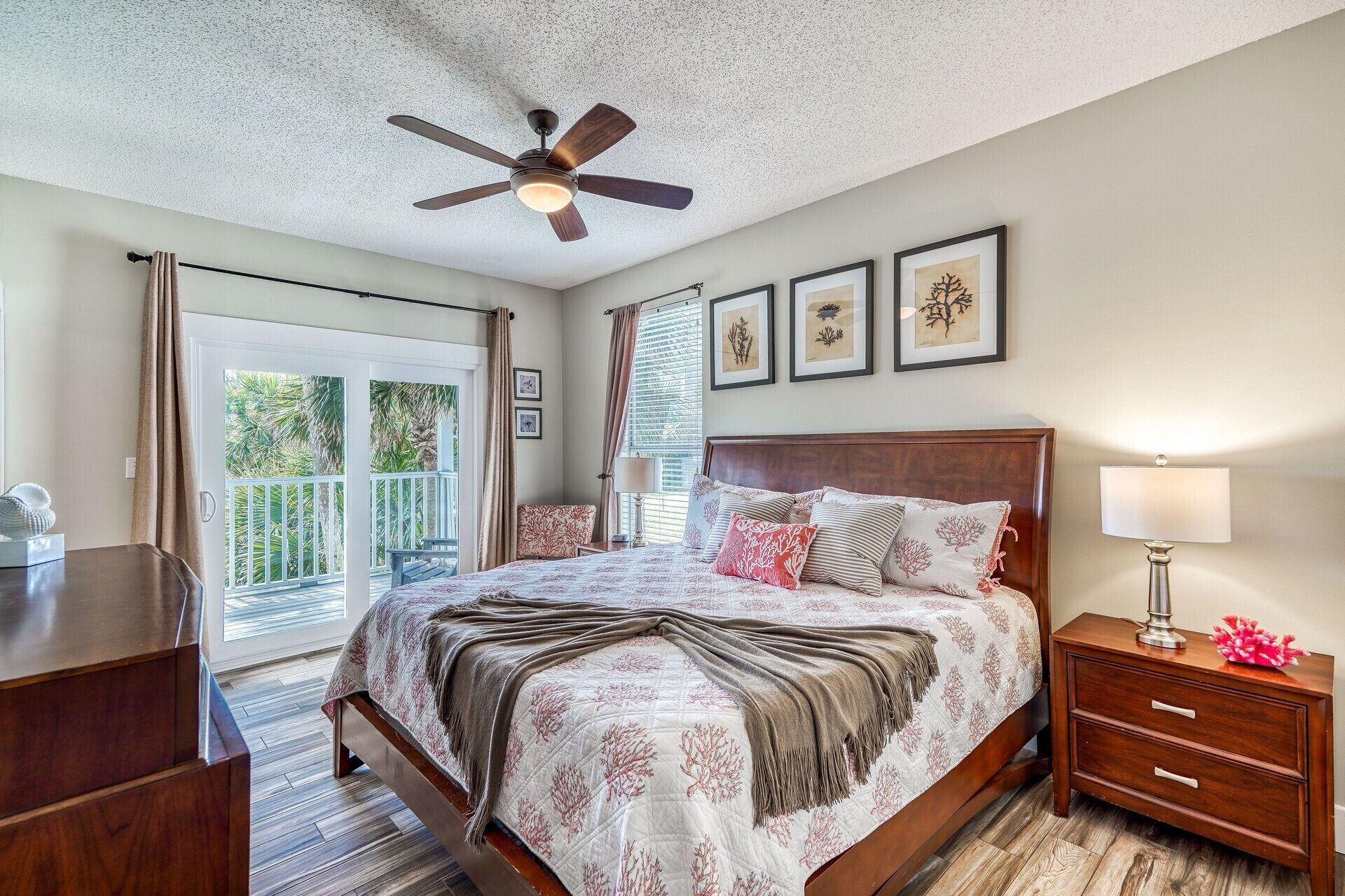 A bedroom with a bed, a nightstand, a ceiling fan, and a window with a view of palm trees.