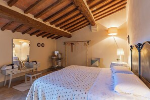 Un dormitorio con techo de madera, una cama con ropa blanca, una mesita de noche con lámpara y un aparador con toallas.