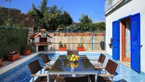 Un espace piscine extérieur avec une table et des chaises en verre, entouré de plantes en pot et d’une clôture en bois.