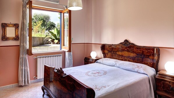 Ein Schlafzimmer mit einem hölzernen Bett, einem Fenster mit Vorhängen, einem Heizkörper und einer Nachttischlampe.