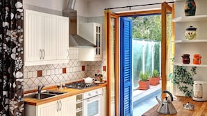 Une cuisine avec des meubles blancs, une cuisinière à gaz et une fenêtre dotée de volets bleus.
