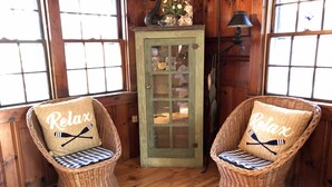 Two wicker chairs with 'Relax' pillows, a green cabinet with glass doors, and a lamp. - Compass Rose Cottage ★ Steps to Flax Pond & Nature Trails ★ Kayaks  (Dennis)